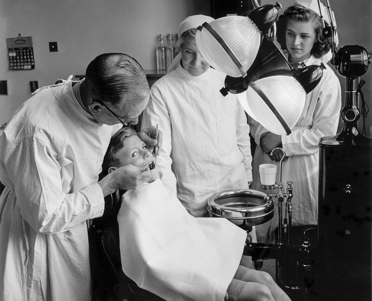Black and white photograph of NHS staff members stood around a young person as they examine their mouth