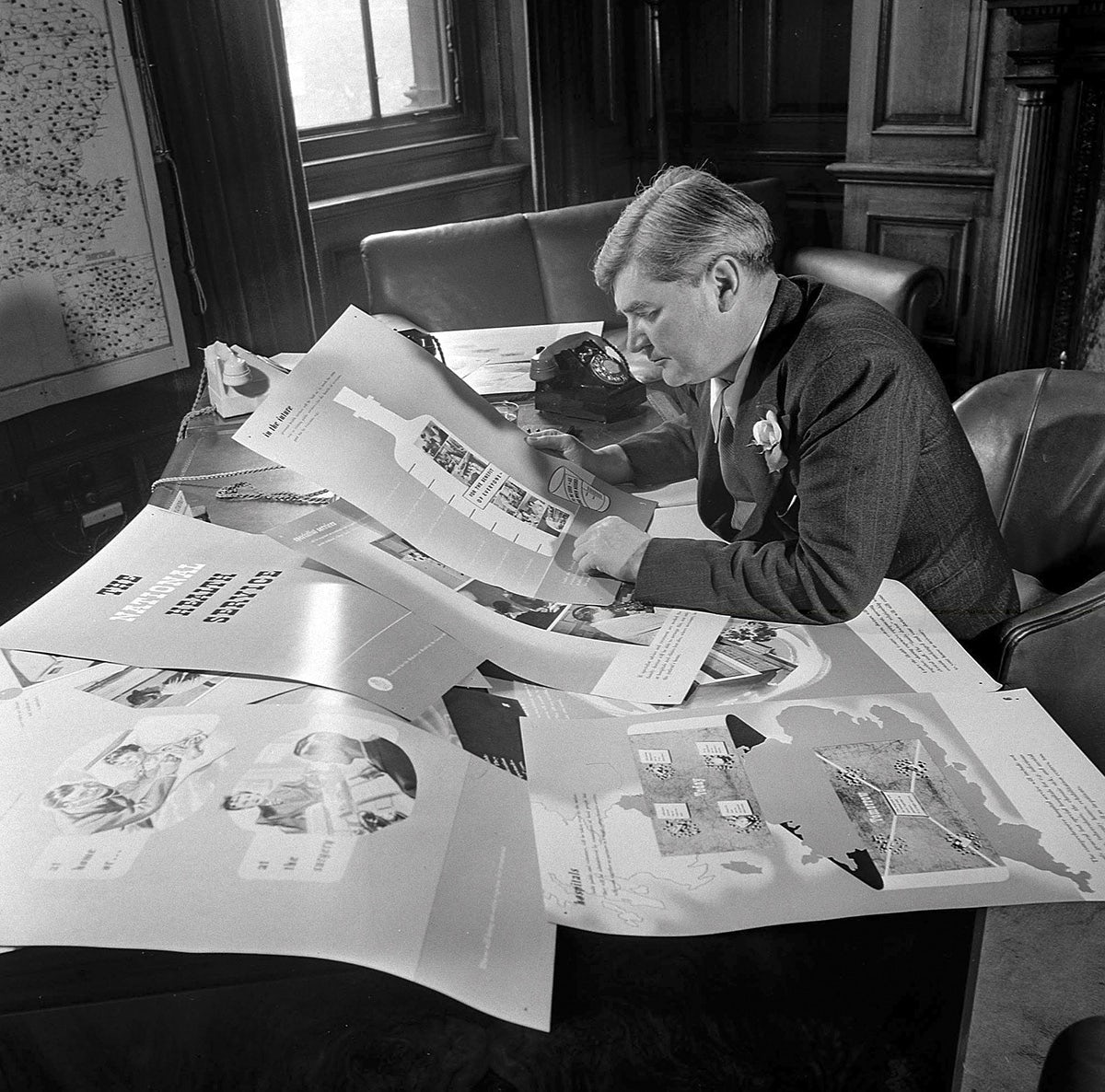 Black and white photograph of Aneurin Bevan, who spearheaded the creation of the NHS, reviewing documents on a table