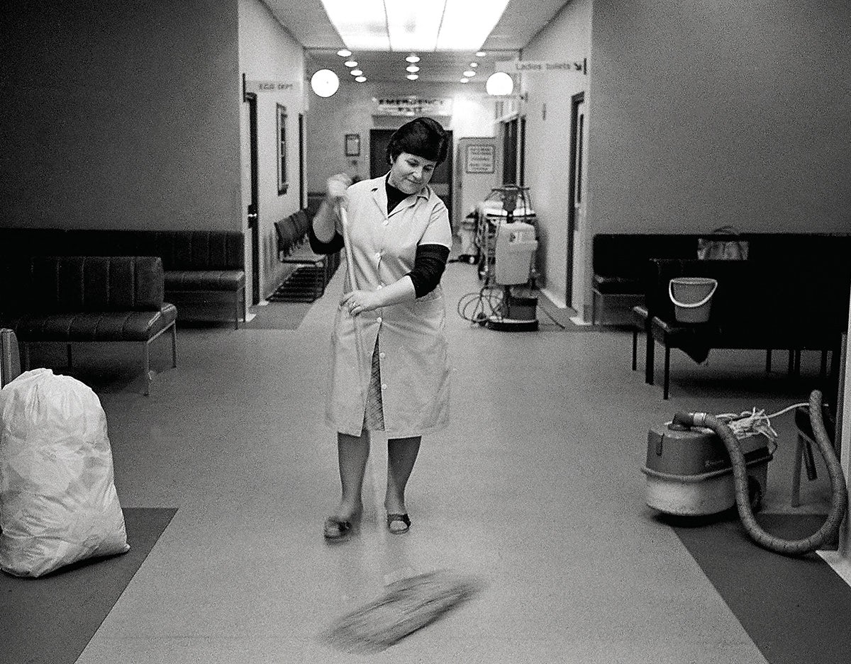 Black and white photograph of an NHS staff member mopping a corridor floor