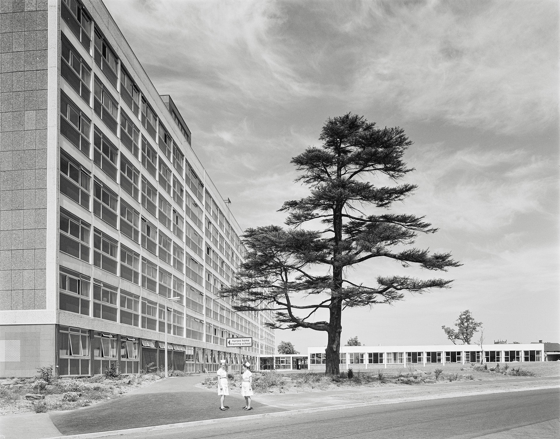 Black and white photograph of a large brutalist hospital building with a tree in front of it