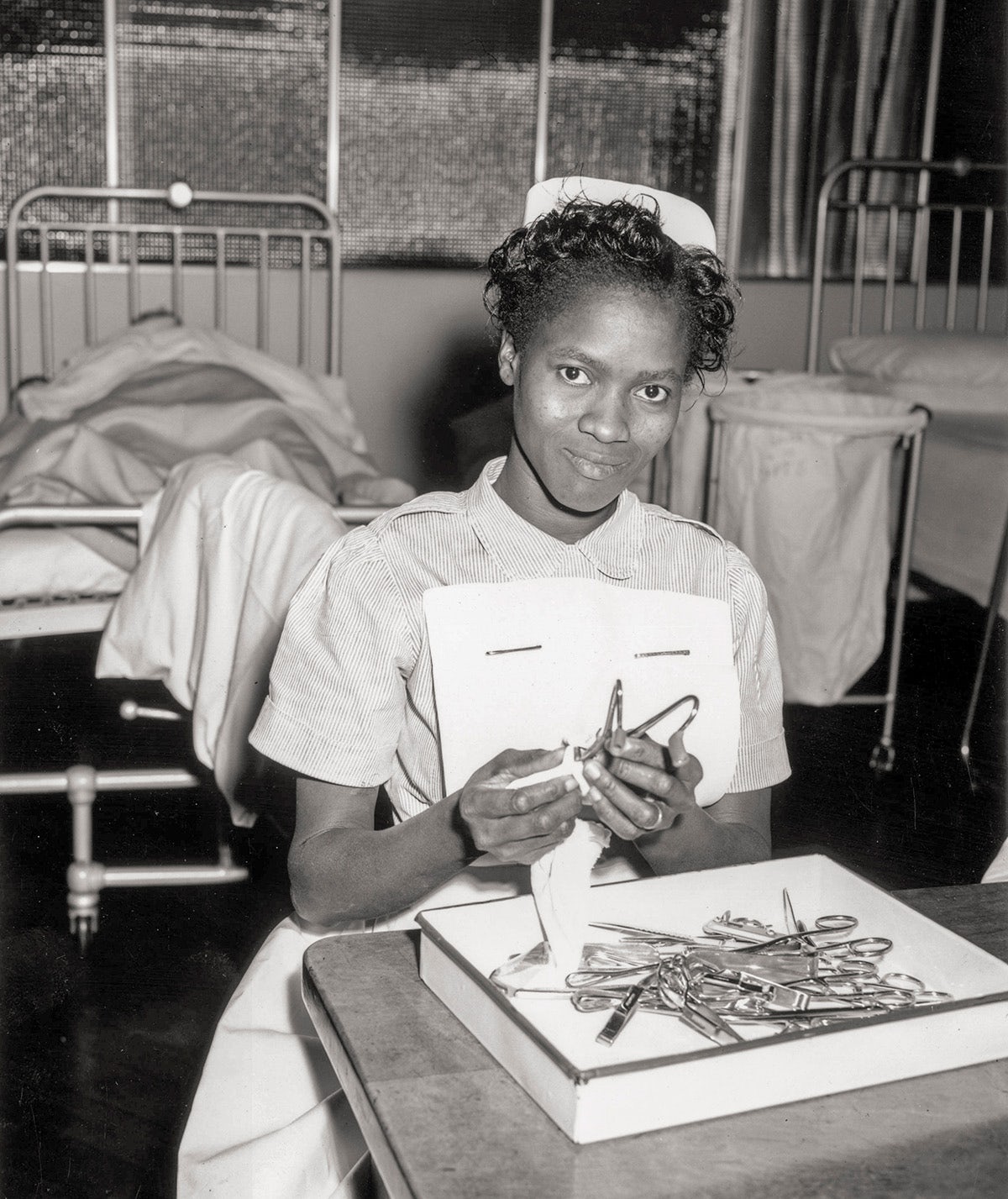 Black and white photograph of an NHS nurse polishing a tray of pincers and other tools